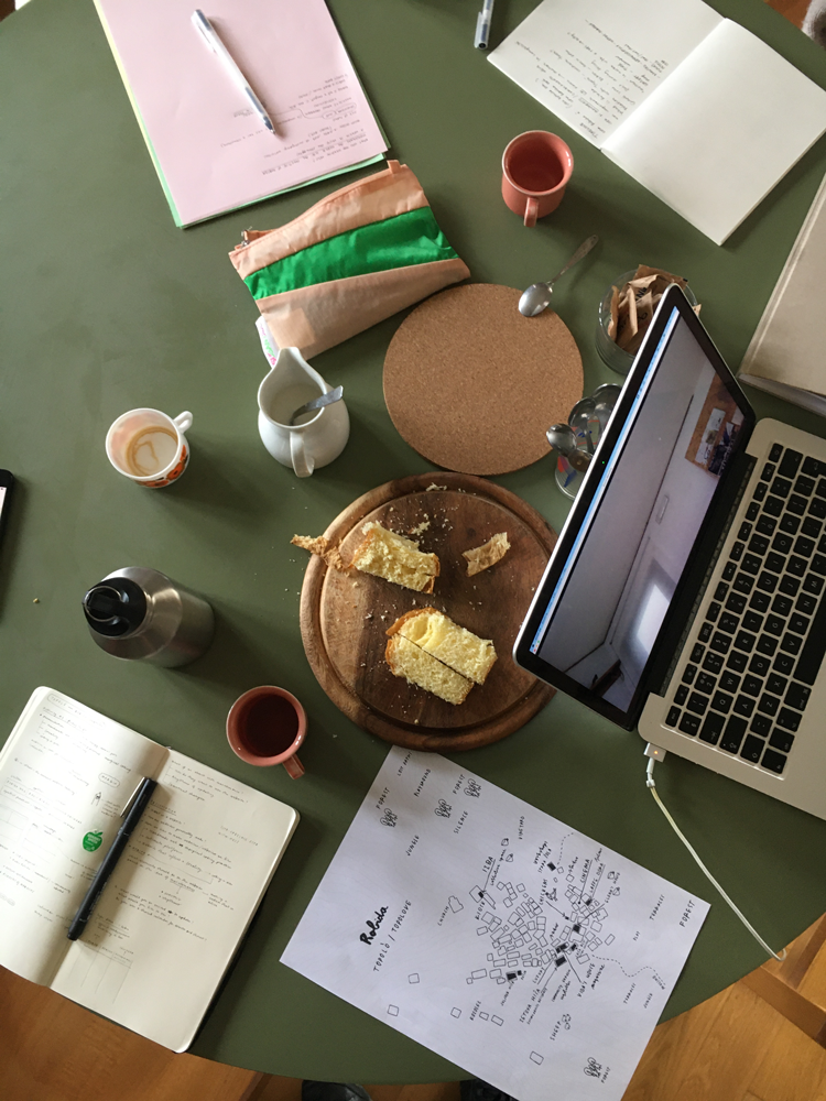 A view of a table from above with notebooks, pens, coffee and cake